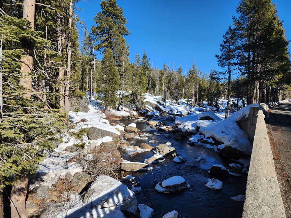 A small mountain river, snow on the boulders and a nice bridge shadow across the river. 