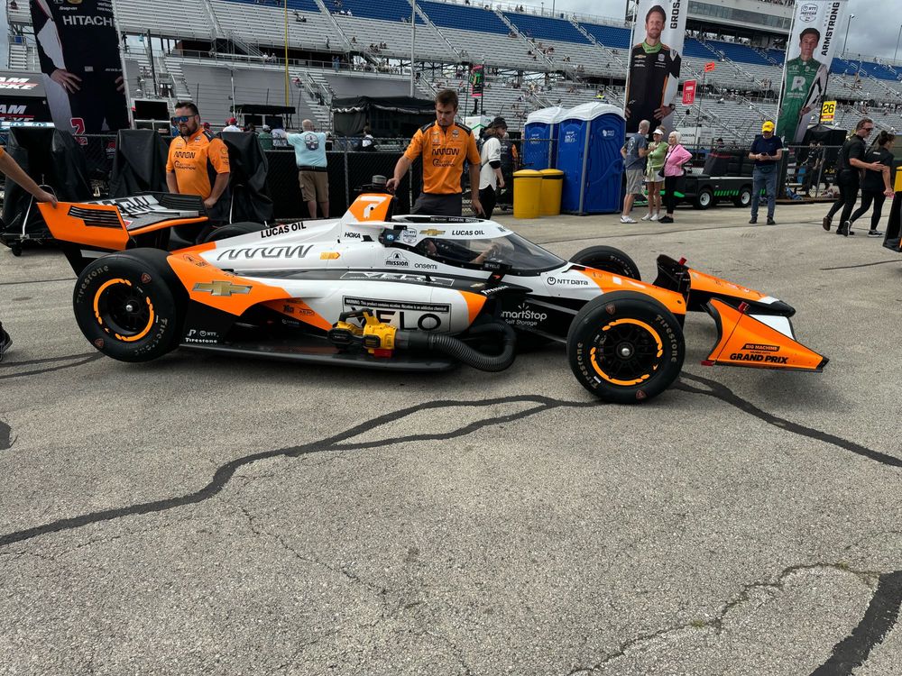 #7 IndyCar in the garage area being rotated around to head out to the pit lane. Orange and white striped racing car. 