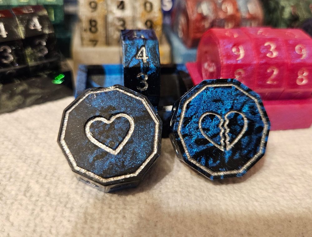 A closeup of the same life counters with two of the coins set aside from the base, displaying the heads and tails hearts