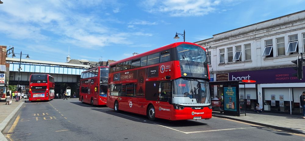Three red double decker buses with railway bridge station behind.