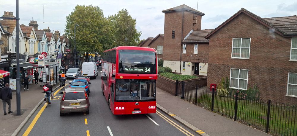 A red double decker bus going up the road.
