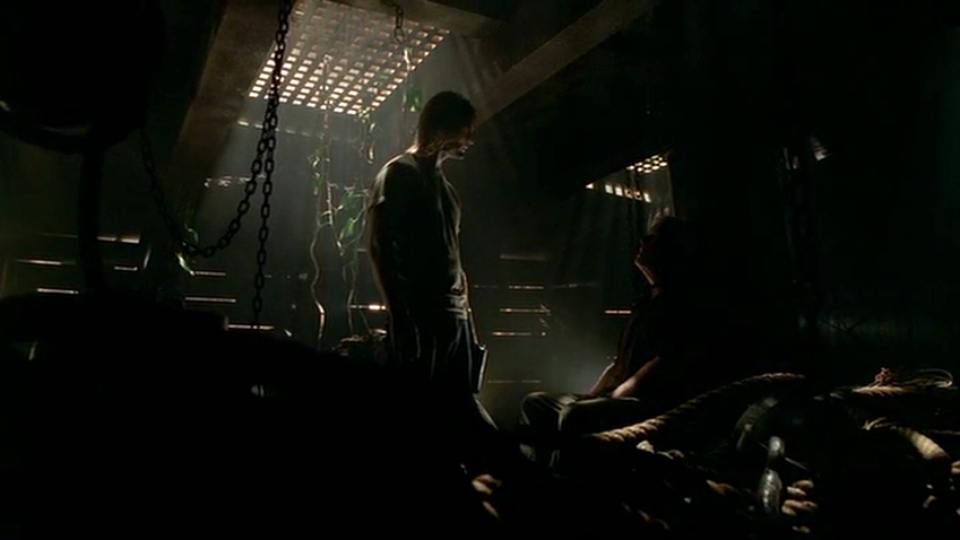 A man standing in a dark room looking at another seated man