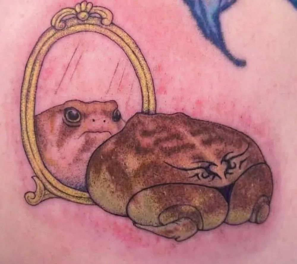 tattoo of a grumpy looking frog staring in a mirror. it is wearing a black thong and has the 