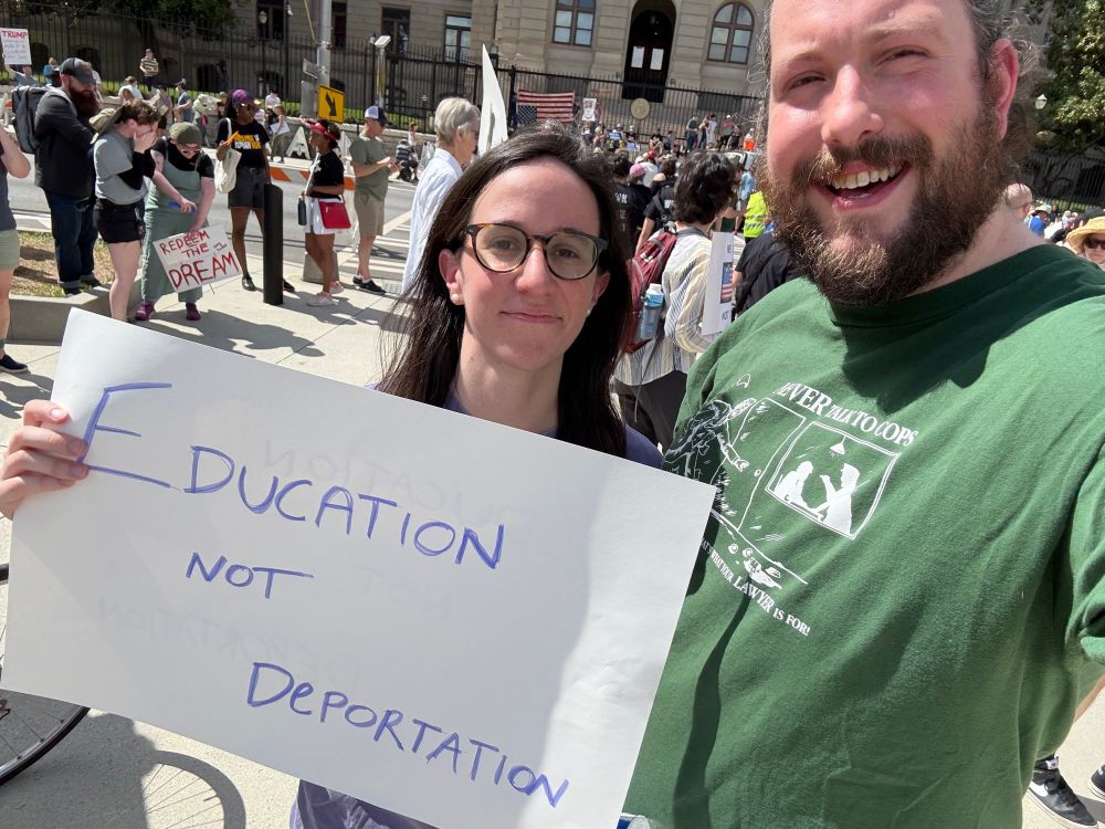 My wife and I standing just outside liberty park in Atlanta. She’s holding a sign that reads “Education Not Deportation” and I’m wearing a T-Shirt that gives instructions for what to say to the police if you are arrested, which is nothing. There are several people holding political signs in the background. 