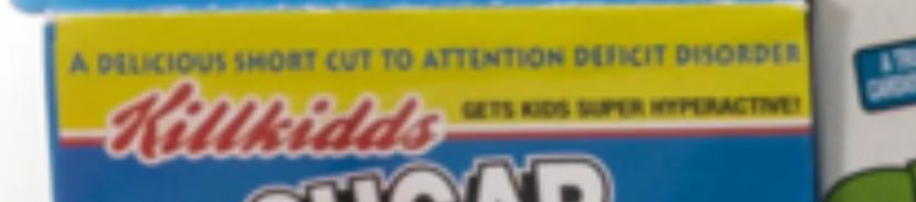 A screenshot of the previous image, zoomed in to show a 'slogan' of one of the parodized cereal boxes. it reads on the yellow border in blue font 'A delicious short cut to attention deficit disorder', and in red kellogg's font, 'killkidds'. In a smaller black font to the right it reads 'Gets kids super hyperactive'.