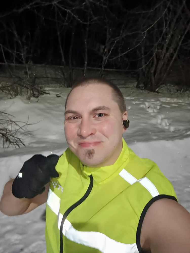 Nuori mies hymyilee ja näyttää littipeukkua ulkona liian vähissä vaatteissa