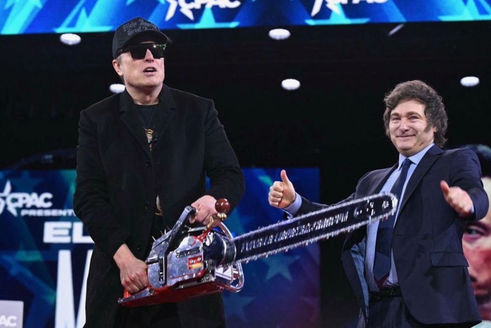 A photo of Elon Musk on stage at CPAC holding a chainsaw presented to him by Javier Milei