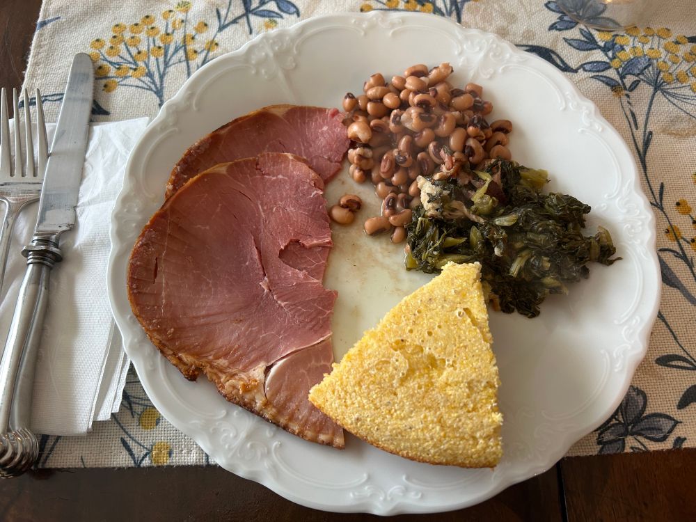 White plate with ham, black eyed peas, turnip greens and cornbread. 