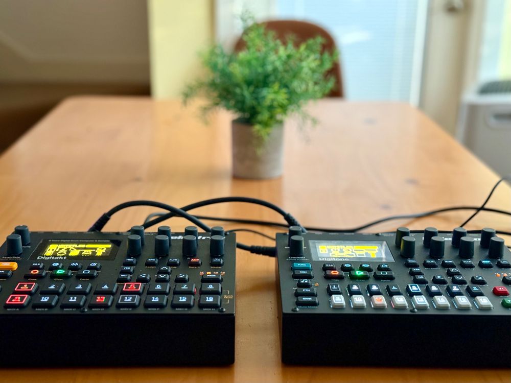 An Elektron Digitakt and Digitone on a wood table with a plant in the background. 
