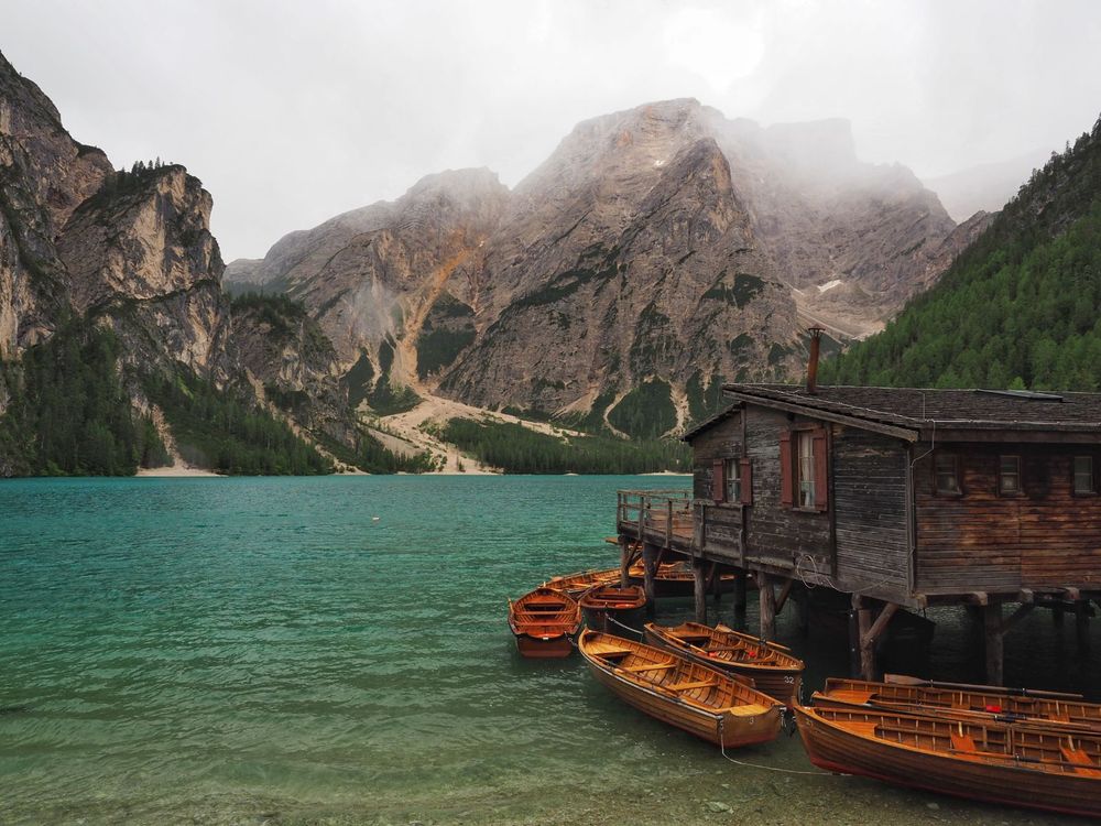 Rowboats and a boathouse on a blue-green lake in front of mountains