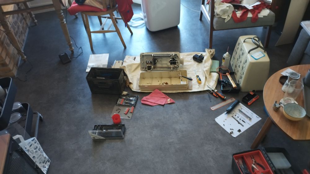 A spread of various tools around an open sewing machine on the floor