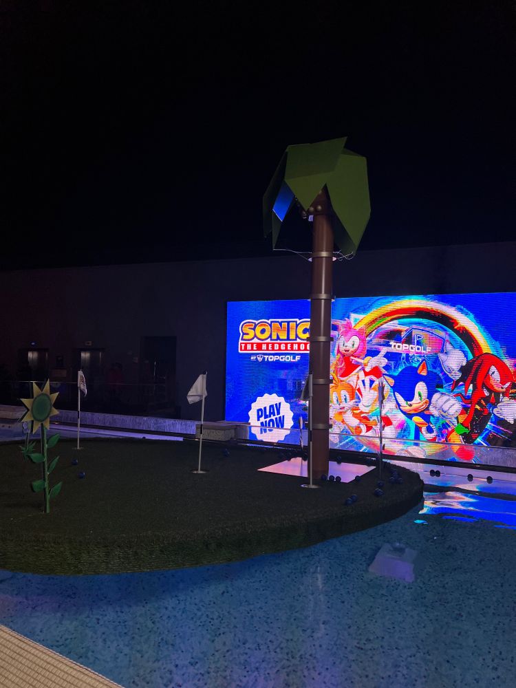 A pool with a floating island with a screen in the back promoting Sonic at Top Golf