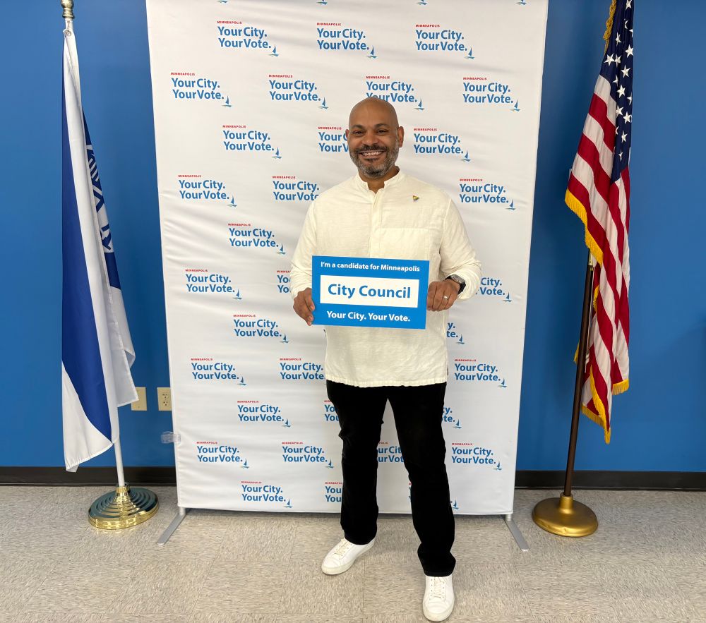 Elliott holding up a sign that says “I’m a candidate for City Council” at the elections and voter services center 