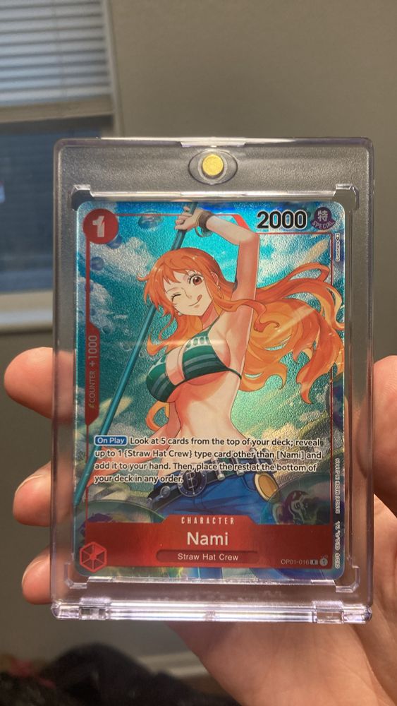 image depicts a trading card of Nami from one piece. She is in her post-timeskip outfit of a blue-green patterned bra and low rise jeans. She is holding her weapon, the Klima-Takt above her head. The textured foiling of the card seems to imply that she has splashed the camera with water