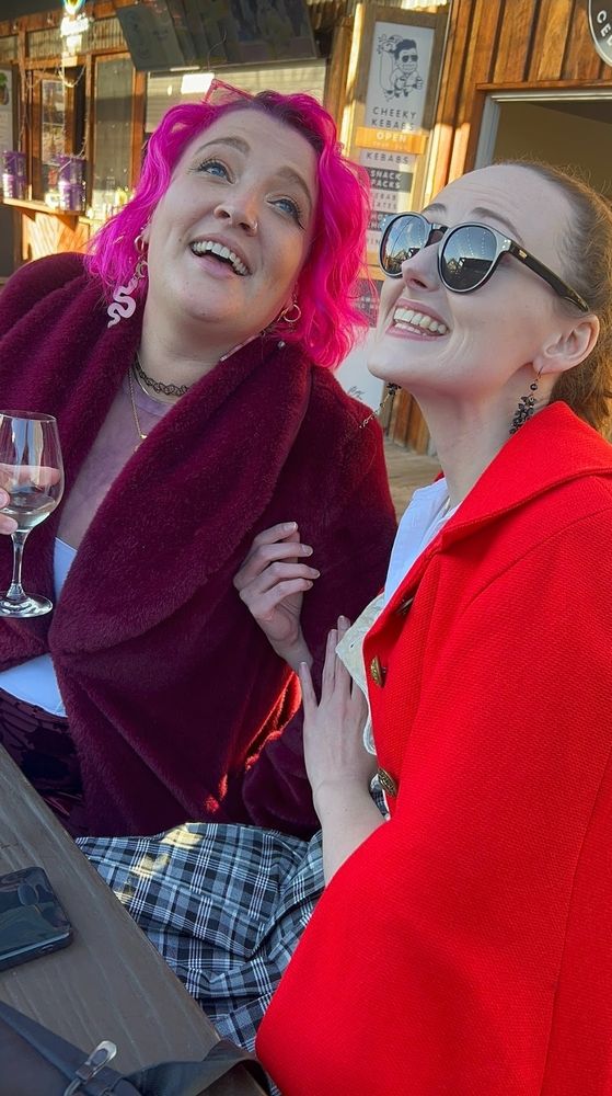 Dael and the same friend later in the day, still holding glasses of wine, but now clinging to each other and singing passionately
