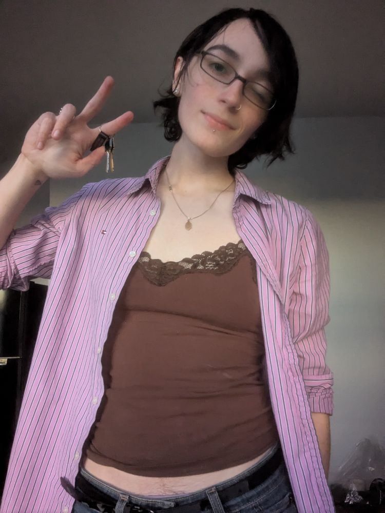 a girl in a brown cami and an unbuttoned pink striped shirt holding a pair of keys and winking at the camera. There is A Reasonable Amount Of Bush Peeking Through tbh