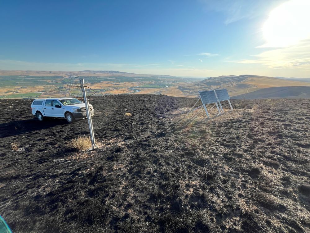 A scenic hill with dark soil and a big sky and a truck parked next to two solar panels.