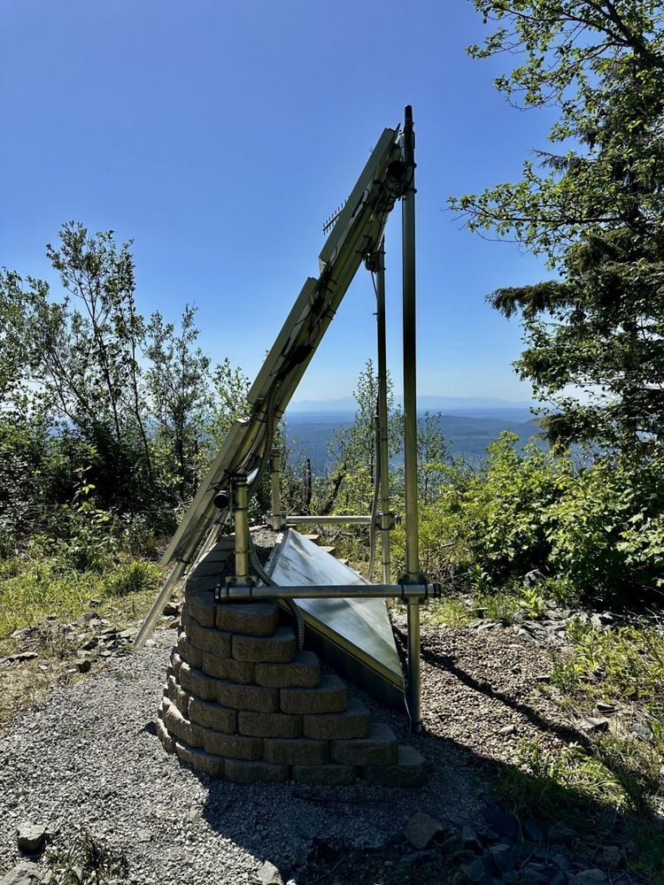 Side view of seismic structure. Paving block wall and gravel in foreground. Green saplings and blue skyline in background. 