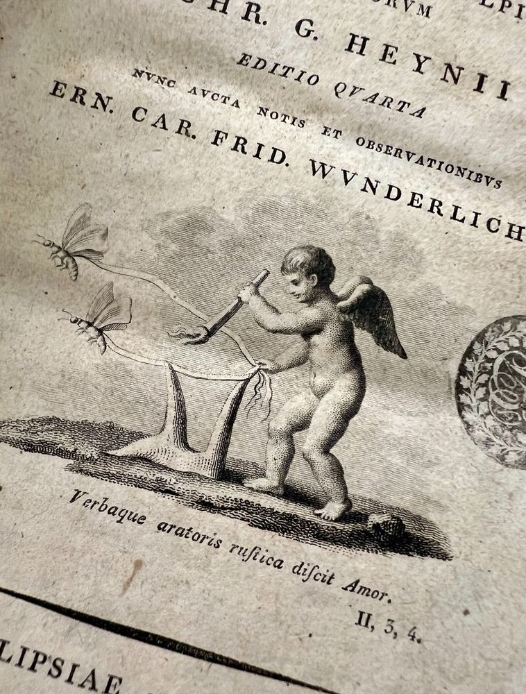 Engraved illustration from an early printed book showing a cherub-like figure with wings holding a small plow and guiding a curved branch or ribbon that appears to be lassoing two butterflies. Below the image, a Latin inscription reads: ‘Verbaque aratoris rustica discit Amor,’ which translates to ‘And Love learns the rustic words of the plowman.’ The book’s title and author information are partially visible, printed in a classic serif typeface.