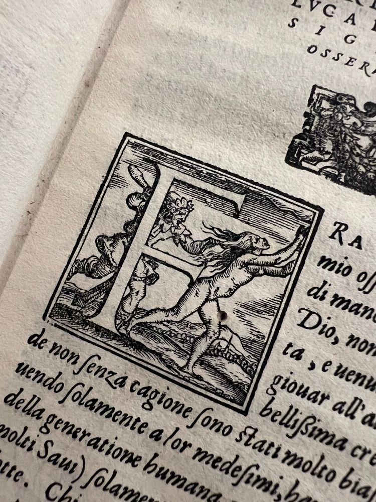 Ornamental initial “F” from an early printed book, depicting a dramatic scene of a woman fleeing while being chased by a male figure in a landscape setting