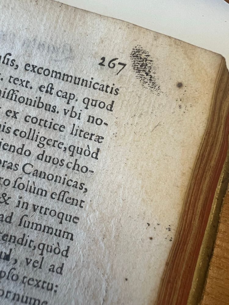 A close-up photo of an old book page numbered 267, showing Latin text printed in black ink. In the upper right margin, there is a visible black fingerprint smudge, suggesting someone with ink-stained fingers touched the page. The paper has a rough texture and slightly browned edges.