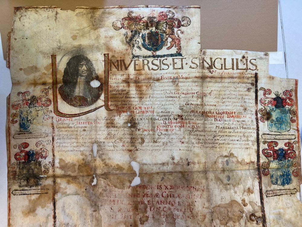 A historic parchment document confirming the nobility of the Scottish Gordon family, featuring ornate calligraphy, coats of arms, a portrait of King Charles IĮ, and decorative elements. The document shows signs of aging and water damage