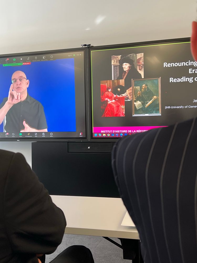 The left screen features a sign language interpreter against a blue background, providing live interpretation. The right screen displays a presentation slide titled “Renouncing Erasmus? Reading…” with images of historical figures
