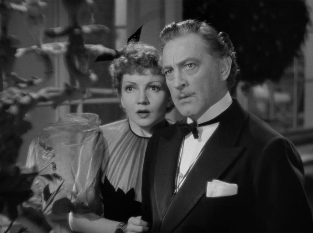 Claudette Colbert looks startled and John Barrymore stern, both in exquisite evening wear in MIDNIGHT (1939)