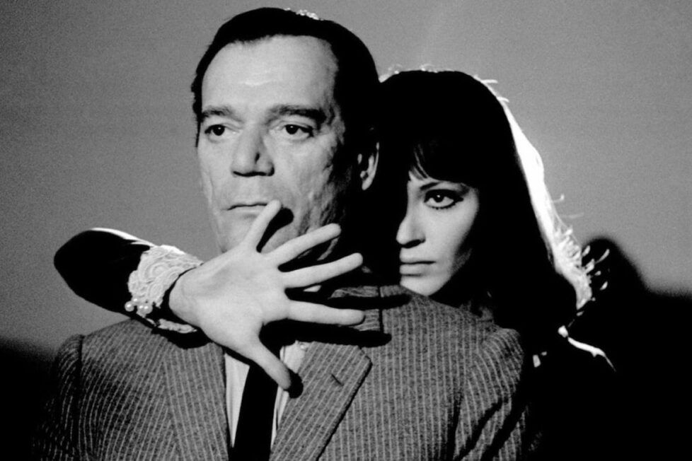 Eddie Constantine and Anna Karina in Aphaville. He’s a heavyset man with a deadpan expression, she’s behind him, her hand in front of his face, backlit like the perfect film noir femme fatale.