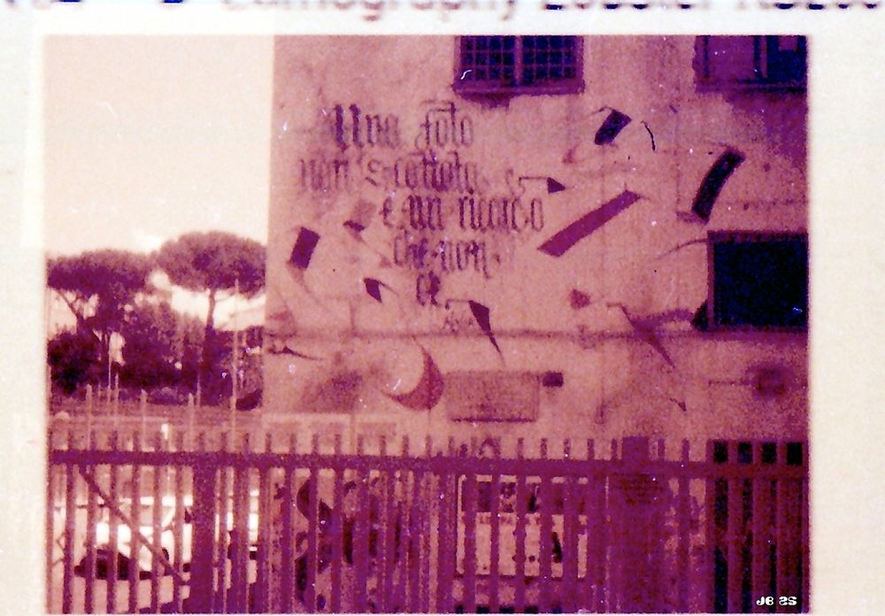 Lo-Fi redscale photo of a building in Rome with a quote written on the wall.