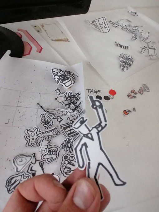 The photos show sections of a first paper prototype of the game ‘My Grandma(88)’. These are hand-drawn and then cut-out NPCs and objects with which the human game master could let the players interact.

I hold one of the cut-out characters in the foreground, while other cut-out objects lie on the table in the background.  