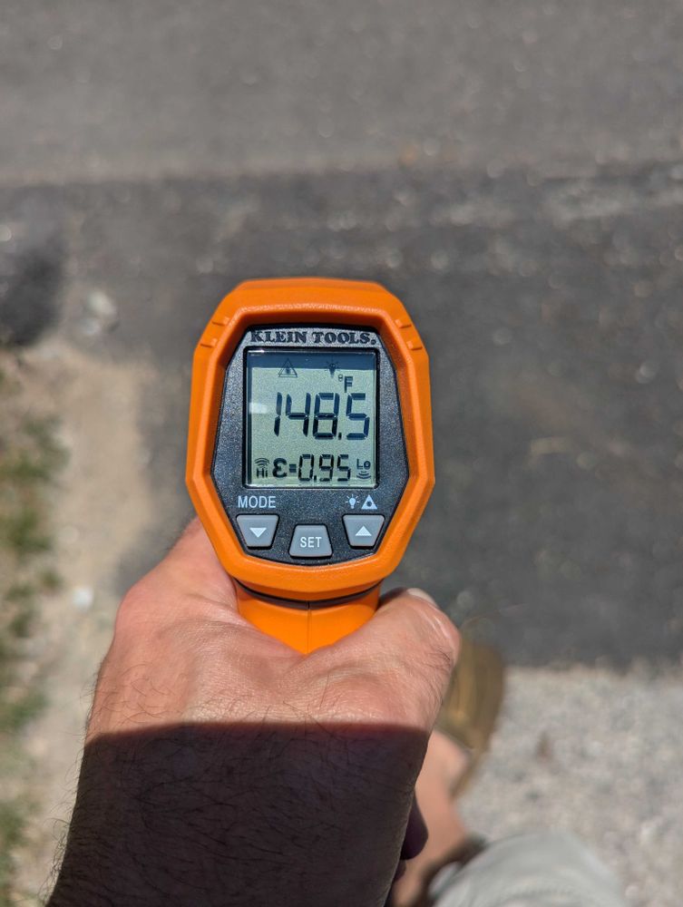 A temperature gun pointed at the pavement. It reads 148.5 degrees.
