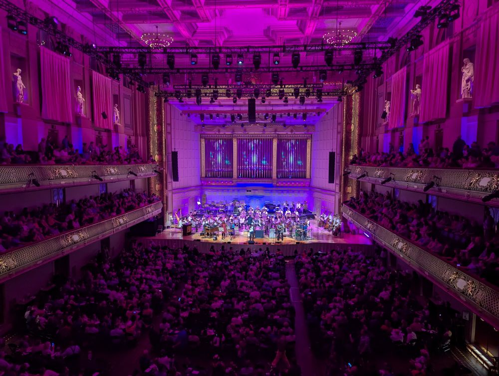 Boston's Symphony Hall lit up in purple. It's a far view to the stage from the second balcony. The Boston Pops are on stage with six other musicians.
