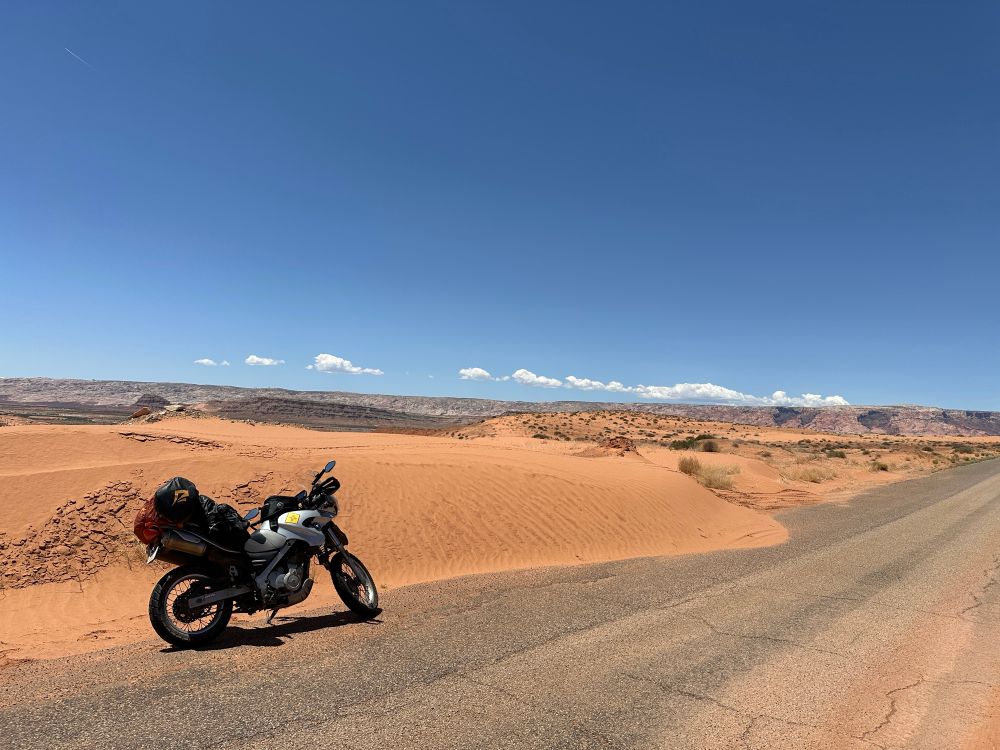 A BMW motorcycle parked next to a red sand dune under blue skies.