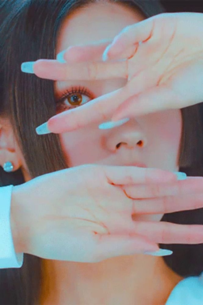 a woman covering her face with her hands with long white nails