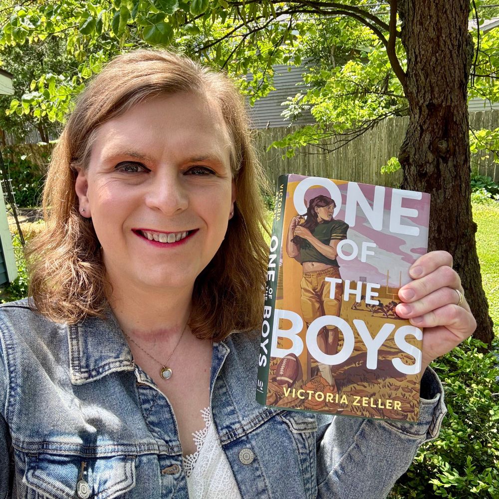 A woman with a jean jacket holding up a copy of Victoria Zeller’s book One of the Boys.