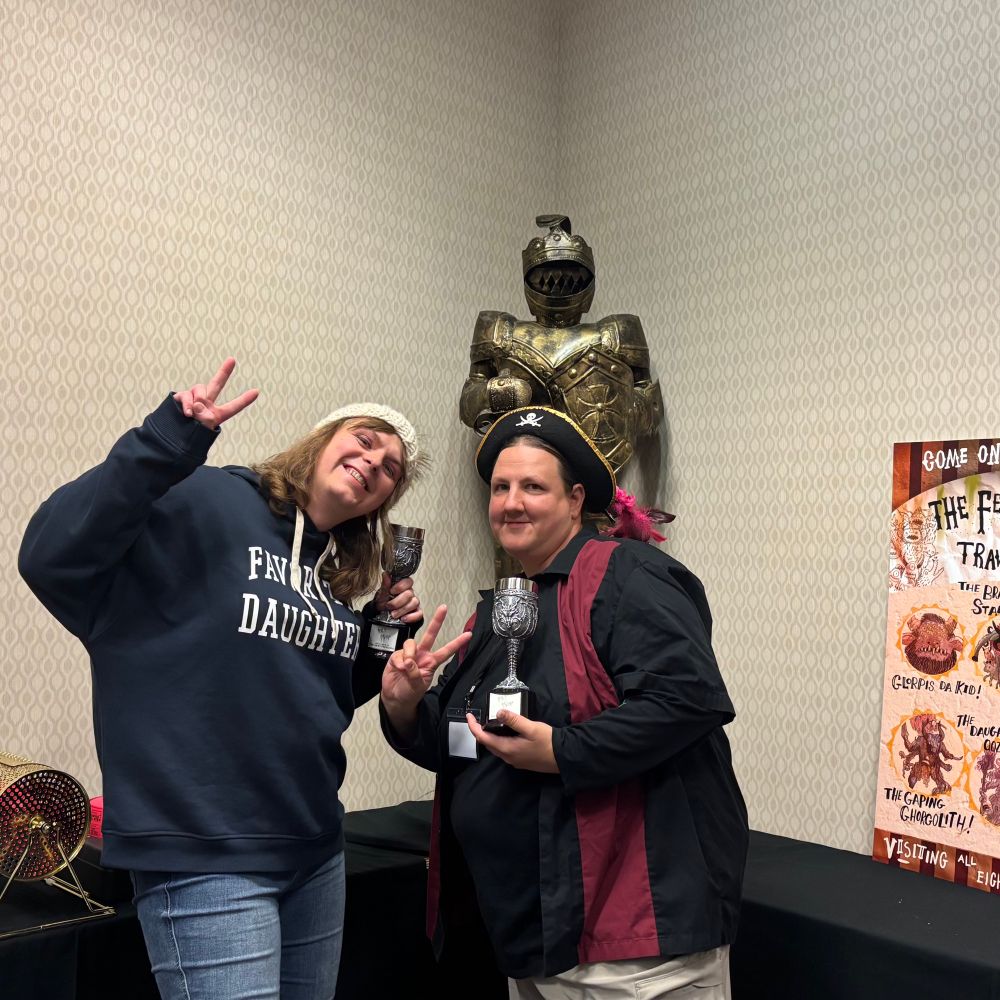 Tori and Tanya holding their Age of Sigmar trophies in front of the holy wars knight.