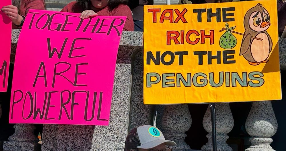 One sign says “together we are powerful” the other says “tax the rich not the penguins