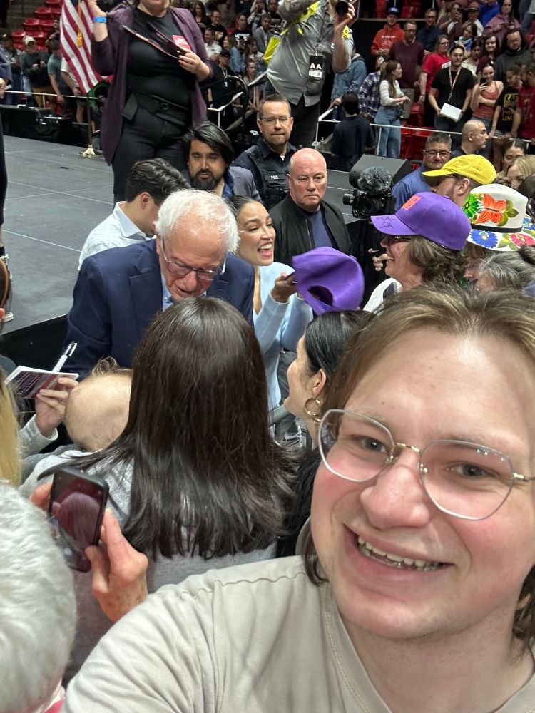 Selfie of Ben Peck with Bernie Sanders and Alexandria Ocasio-Cortez right behind him meeting with people