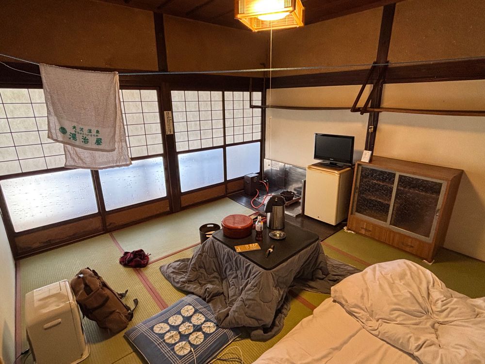 宿の八畳間。こたつと簡単な自炊設備。物干し用のロープが吊ってある。