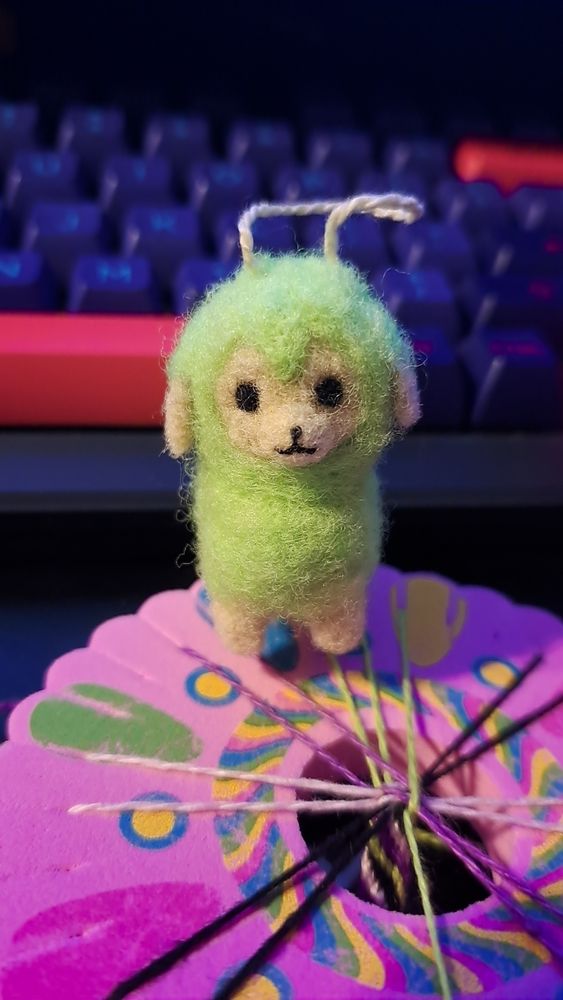 a photo of a small needlefelted alpaca with green wool.