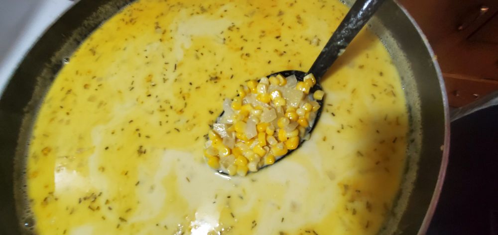 Ladleful of vegetables lifted out of a pot of corn chowder