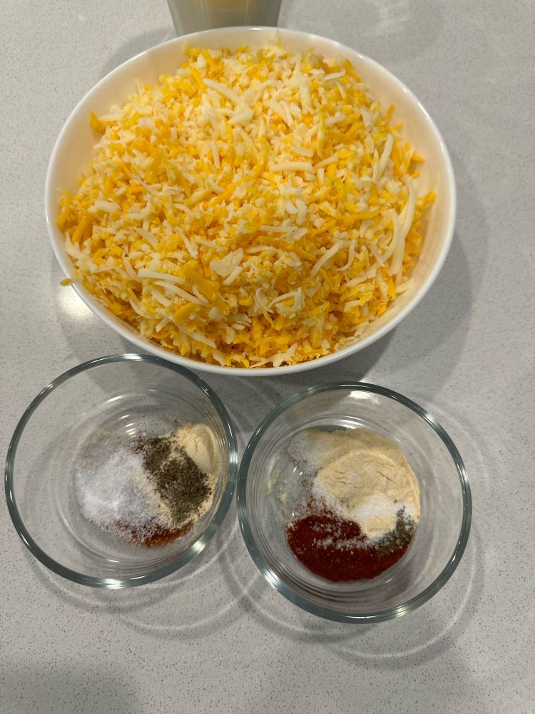 A big bowl of shredded cheese and two small cups of seasoning.