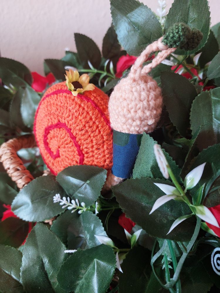 Crochet Snail Amigurumi sitting in basket full of green leaves