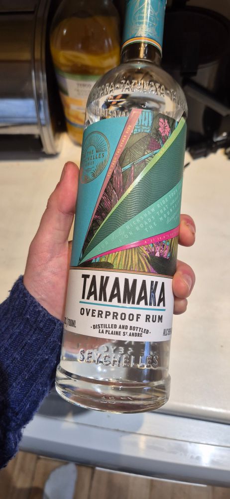 A picture of a bottle of takamaka overproof rum, green label, colourless label and liquid