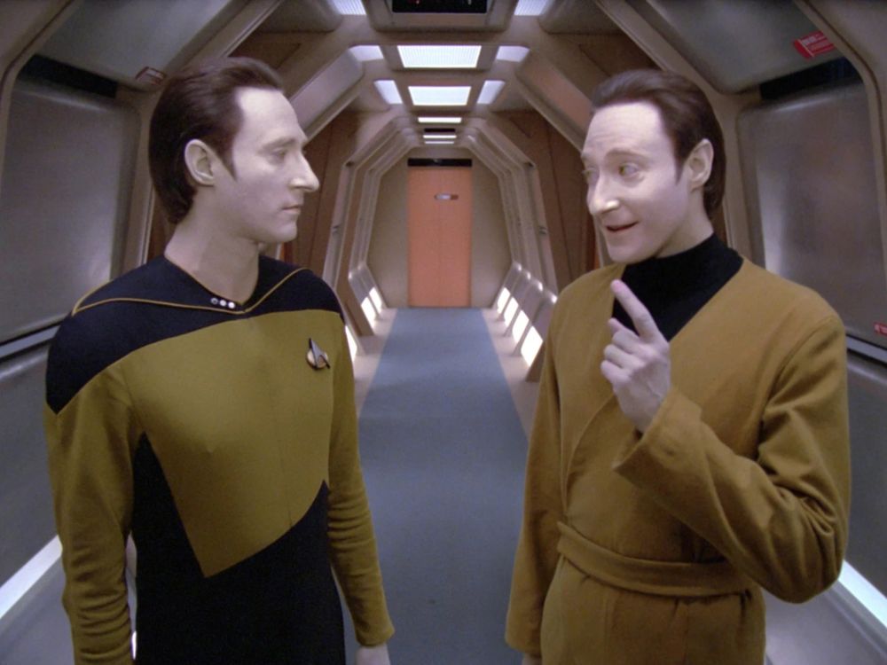 Data and lore, two characters from Star Trek the next generation, both played by Brent Spinner, stood in a corridor in conversation 