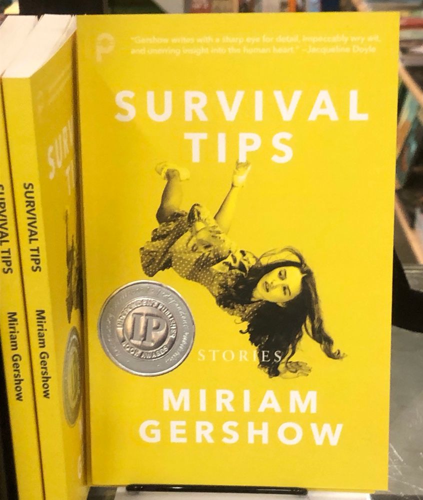 A bright yellow cover of Survival Tips beside two copies with spines out on the shelf of The Propeller Store. 