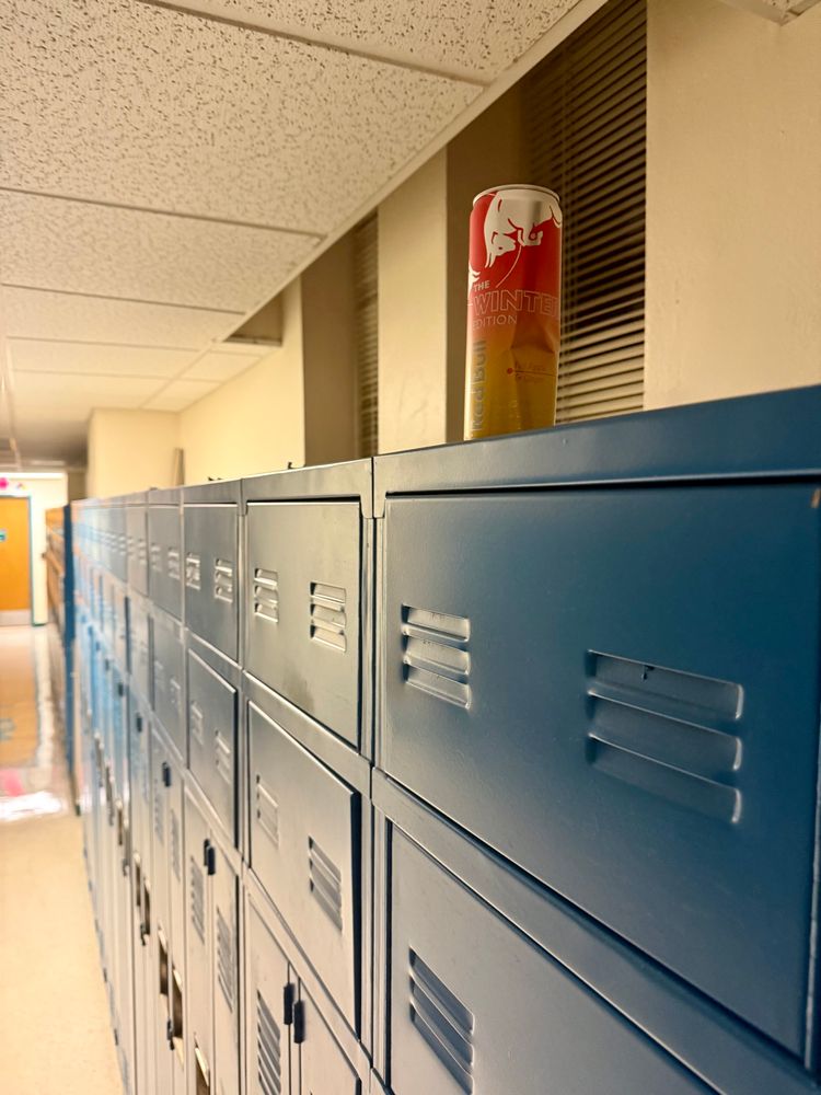 a full but open 12oz red bull winter edition can sits atop a row of blue metal lockers in a hallway. 