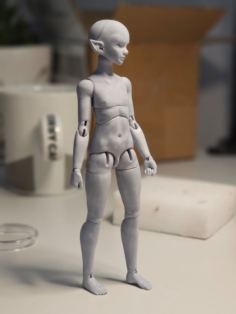 A small grey doll with elf ears is standing on a table and looking to the right.