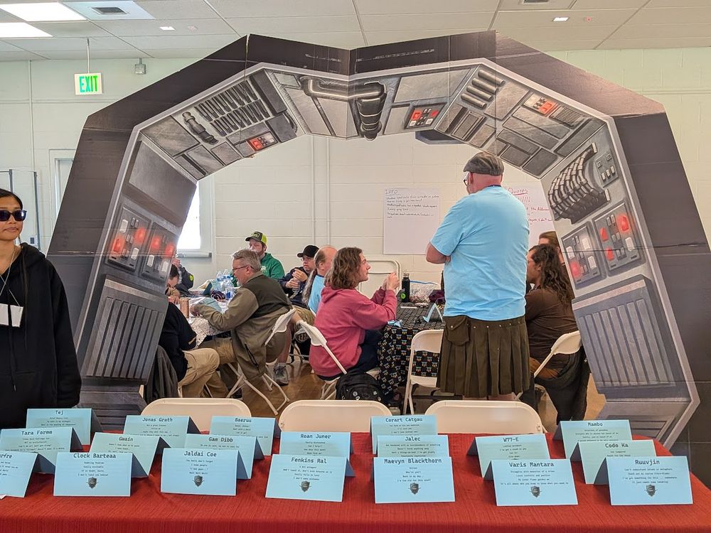 Freebooters character tents on a table in front of a Star Wars themed arch.  People are playing a tabletop RPG on tables in the background.